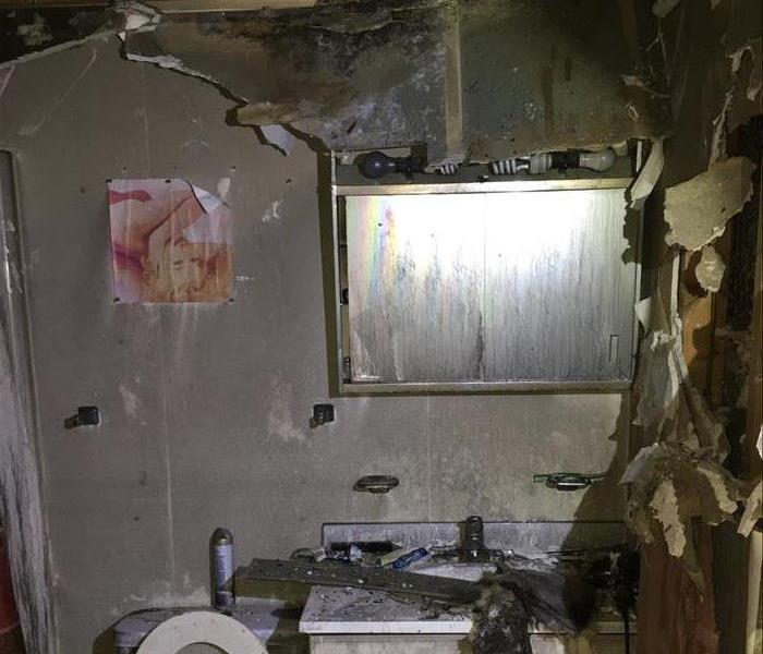 Bathroom sink, and mirror that is damaged by a fire. The ceiling is collapsed and the walls are covered in soot and water