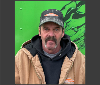 Man in SERVPRO hat mustache and beard wearing a Sweatshirt with bright green background